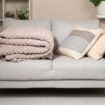 Moderná sivá sedačka s pletenou prikrývkou a vakúšmi.