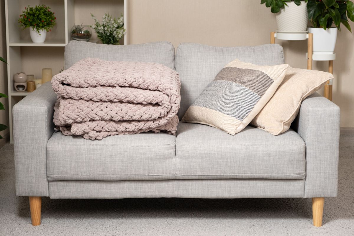 Moderná sivá sedačka s pletenou prikrývkou a vakúšmi.