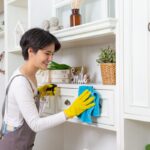 Žena utiera prach z nábytku handrou a prípravkom v spreji.