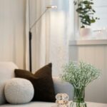 Svetlý konferenčný stolík s bielou mramorovou podložkou, sklenenou vázou s drobnými kvetmi a čiernym textilným vankúšom.