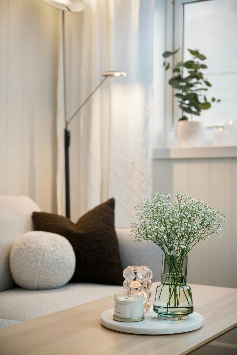 Svetlý konferenčný stolík s bielou mramorovou podložkou, sklenenou vázou s drobnými kvetmi a čiernym textilným vankúšom.