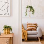 Drevená retro komoda s dizajnovou stolnou lampou, zelenou rastlinou v žltom kvetináči a abstraktným lineárnym obrazom.