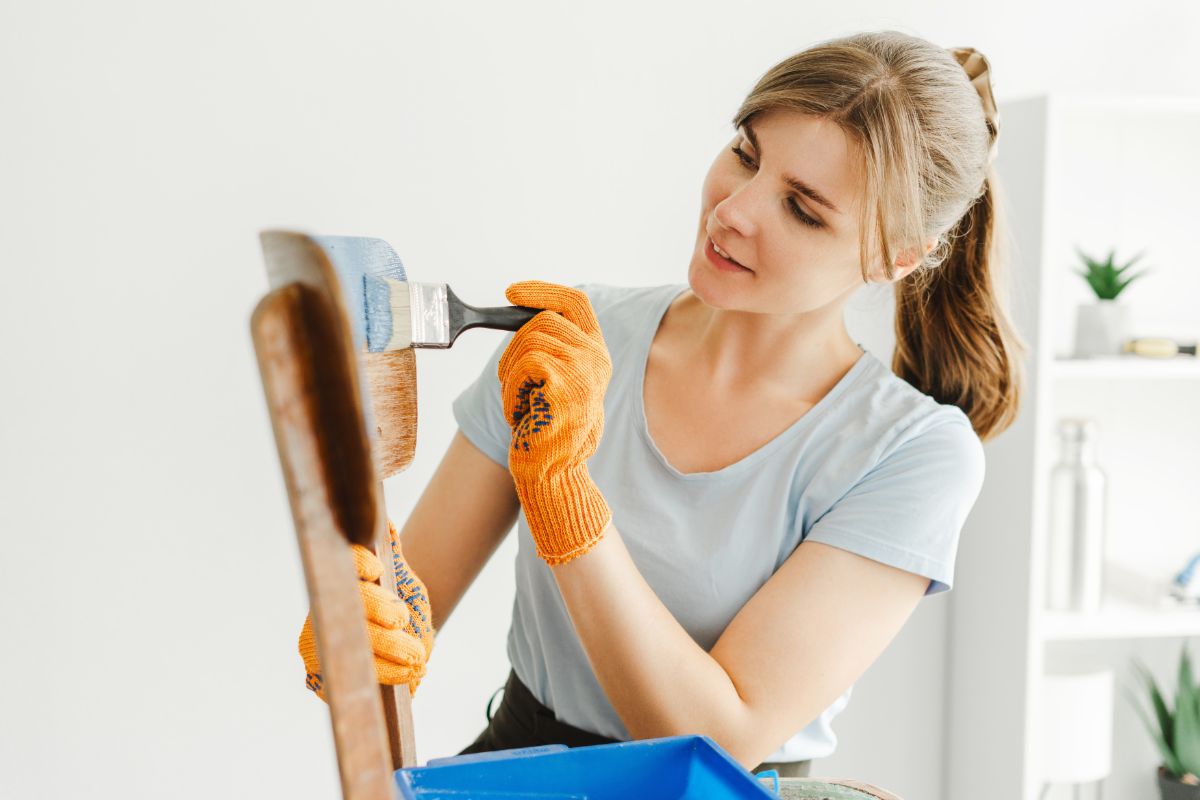 Žena pri natieraní stoličky farbou.