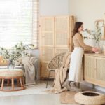 Žena upravujúca vázu v svetlej obývačke s ratanovým nábytkom.