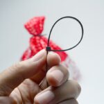 Detail na ruku držiacu sťahovaciu pásku, v pozadí vrecko stiahnuté sťahovacou páskou.