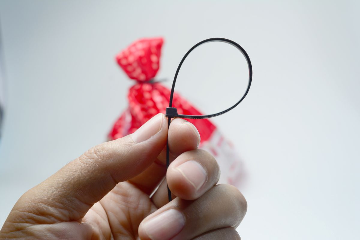 Detail na ruku držiacu sťahovaciu pásku, v pozadí vrecko stiahnuté sťahovacou páskou.