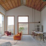 Otvorená obývacia izba s oranžovou sedačkou, vysokým stropom s tehlovým obkladom a veľkými oknami.