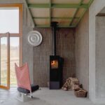 Čierne krbové kachle pred hnedou štruktúrovanou stenou pod zelenou oceľovou konštrukciou galérie.