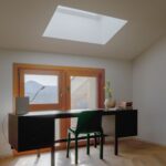 drevený písací stôl so zelenou stoličkou pod strešným oknom v podkrovnom interiéri.