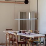 Dlhý svetlý drevený stôl na žltých kovových podnožiach s rôznymi retro stoličkami v jedálni.