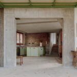 Kuchyňa so zelenými skrinkami a kamennou stenou v surovom betónovom ráme.