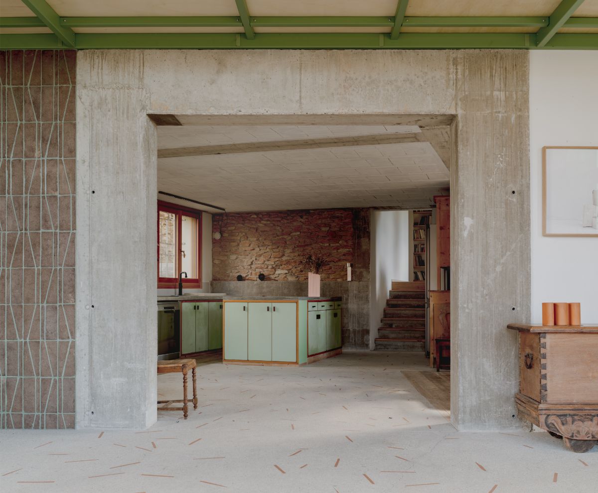 Kuchyňa so zelenými skrinkami a kamennou stenou v surovom betónovom ráme.