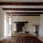 radičný murovaný krb v bielej miestnosti s tmavými drevenými trámami.