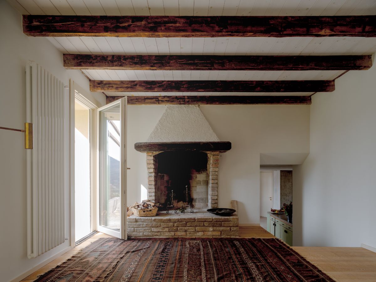 radičný murovaný krb v bielej miestnosti s tmavými drevenými trámami.