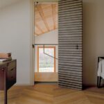 Moderné vzorované dvere v bielej stene nad drevenou podlahou so vzorom rybej kosti.