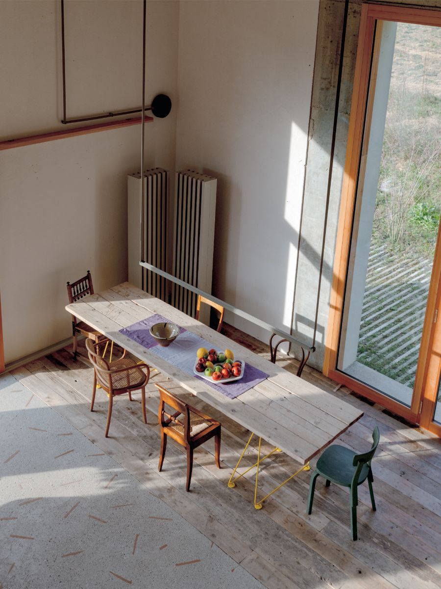 Drevený jedálenský stôl s rôznymi drevenými stoličkami v interiéri domu s drevenou podlahou.