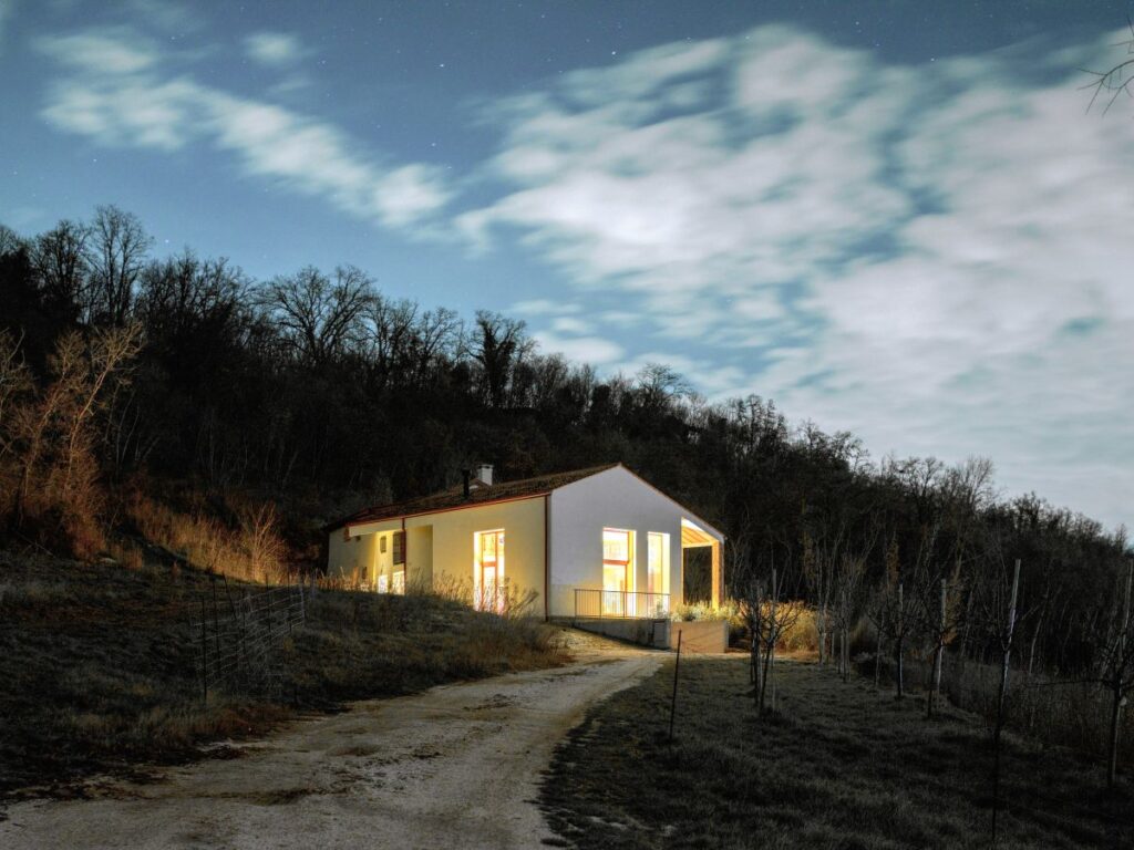 Biely jednopodlažný dom so sedlovou strechou a veľkými presklenými oknami v kopcovitom teréne.