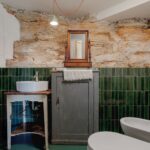 Kúpeľňa s tmavozeleným obkladom, kamennou stenou, sivou skrinkou a umývadlom na stolčeku.
