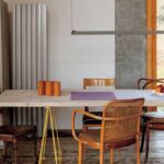 Masívny drevený stôl s rôznymi retro stoličkami pri vysokom okne.