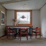 Modrý okrúhly stôl s červenými drevenými stoličkami pod oknom v retro interéri.