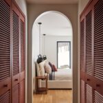 Pohľad z chodby so vstavanými skriňami do spálne s posteľou so svetlou posteľnou bielizňou a vankúšmi.