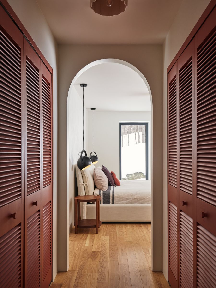 Pohľad z chodby so vstavanými skriňami do spálne s posteľou so svetlou posteľnou bielizňou a vankúšmi.