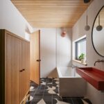 Kúpeľňa s grafickou čiernobielou dlažbou, dreveným stropom a červeným umývadlom pri vani.