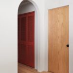 Oblúkový priechod na chodby so vstavanými skriňami s červenými dverami.