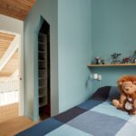 Detská izba so svetlotyrkysovými stenami, drevenou policou a farebnou posteľnou bielizňou.