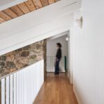 Moderná galéria s bielymi trámami, drevenou podlahou a priznanou kamennou stenou.