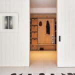 Pohľad na otvorený šatník obložený drevom za bielymi posuvnými dverami v minimalistickej chodbe.