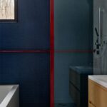 Modrý mozaikový obklad v kúpeľni s červeným kovovým držadlom a svetlou terazzovou podlahou..