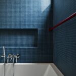 Modrá mozaiková nika nad bielou vaňou s antikorovou batériou a výrazným červeným potrubím.