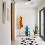 Svetlá predsieň s geometrickou dlažbou, dreveným vešiakom a tyrkysovou dizajnovou stoličkou pri okne.