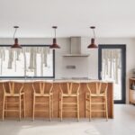 Kuchynský ostrov z prírodného dreva s barovým sedením a bordovými závesnými lampami.