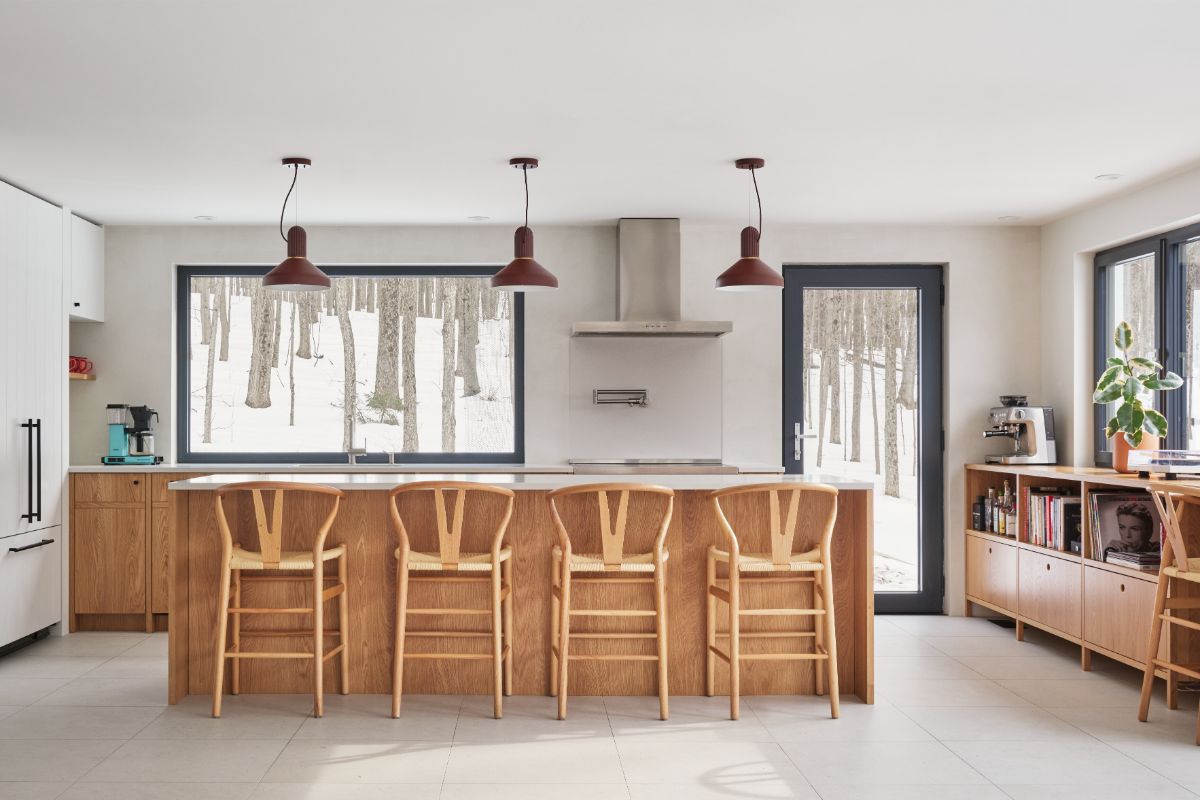 Kuchynský ostrov z prírodného dreva s barovým sedením a bordovými závesnými lampami.