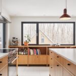 Kuchynská linka s drevenými skrinkami, bielou pracovnou doskou, antikorovým sporákom a drevenou knižnicou pod oknom.