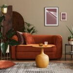 Oranžová zamatová sedačka, žltý kovový stolík, tmavý drevený paraván a veľké zelené izbové rastliny.