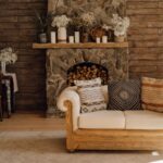 Masívny kamenný krb, drevený obklad stien, biela nízka sedačka a dekoratívne vankúše s etno vzorom.