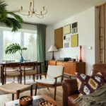 Kožená hnedá pohovka, drevený jedálenský stôl, retro príborník a biele steny s minimalistickými obrazmi.