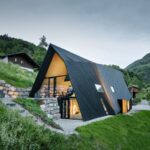 Pohľad na chatu VA House s podsvieteným interiérom a horskou panorámou za súmraku.