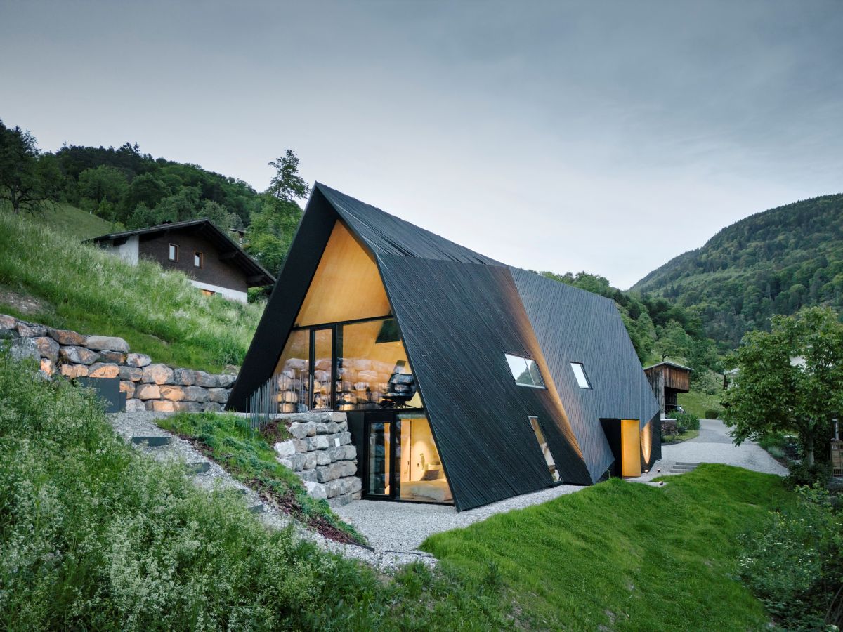 Pohľad na chatu VA House s podsvieteným interiérom a horskou panorámou za súmraku.