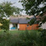 Záhrada so zrekonštruovanou chalupou s drevenou a bielou fasádou a zelenými oknami na vidieku.