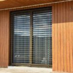 Okno so žalúziami pri drevom obloženej fasáde.