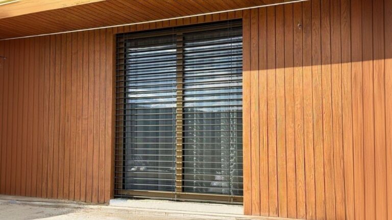 Okno so žalúziami pri drevom obloženej fasáde.