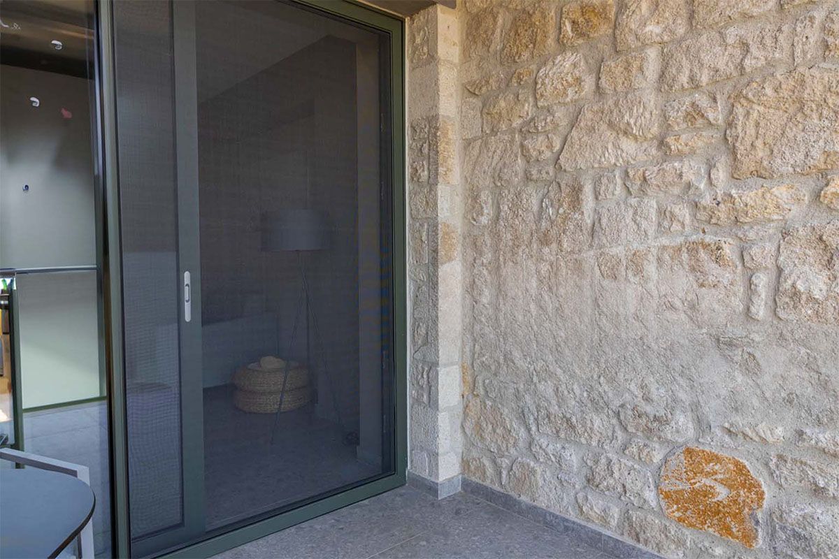 Posuvné vstupné dvere so sieťkou pri surovej kamennej stene.