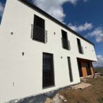 Moderný poschodový dom s rovnou strechou a vonkajšími žalúziami.