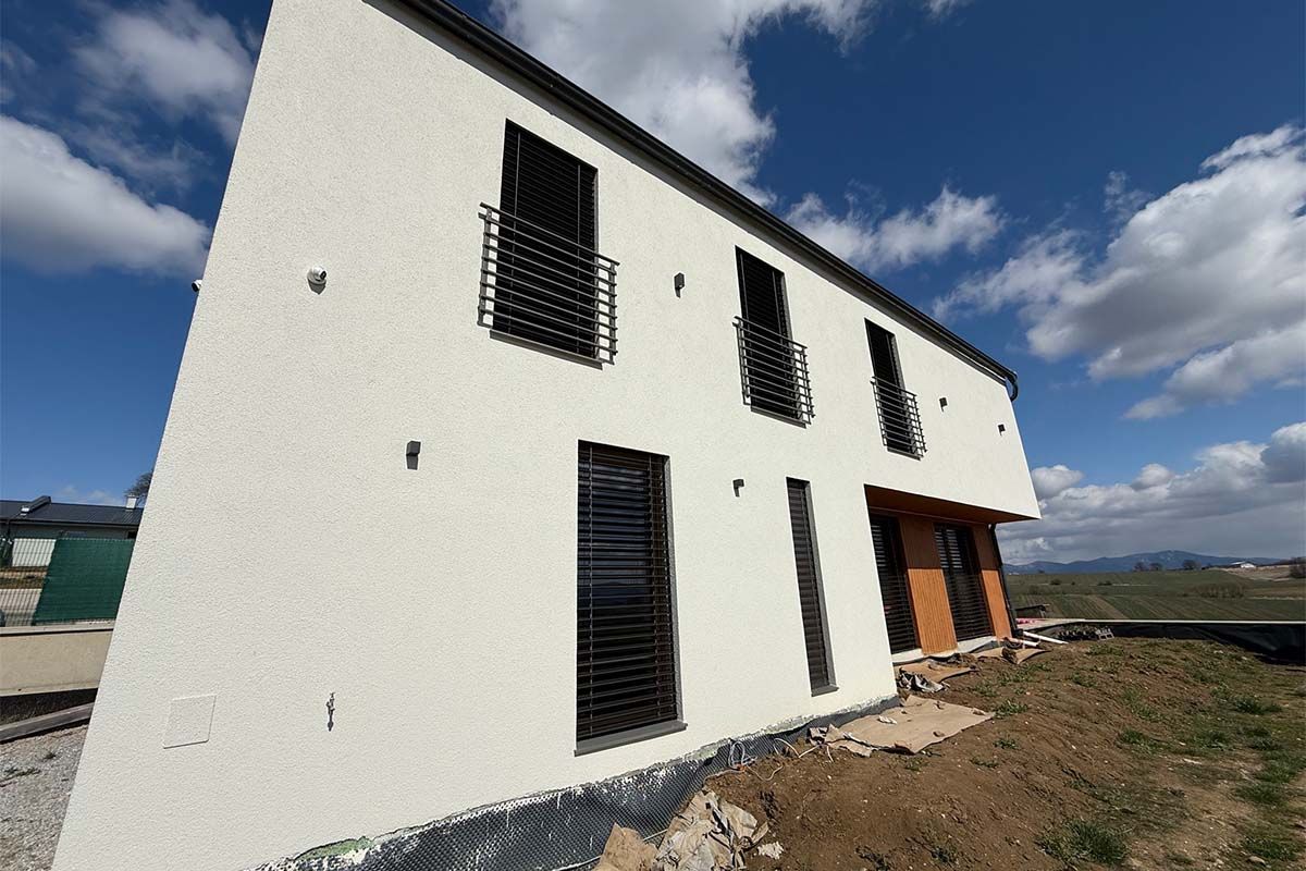 Moderný poschodový dom s rovnou strechou a vonkajšími žalúziami.