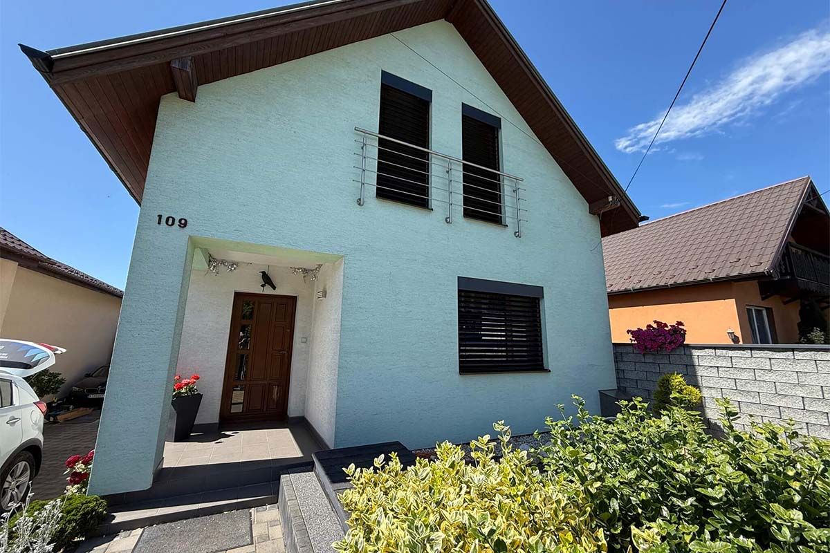 Rodinný dom so sedlovou strechou a vonkajšími žalúziami na oknách.