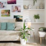 Svetlá menčestrová pohovka s tyrkysovými vankúšmi pod bielou stenou s osobnými fotografiami.